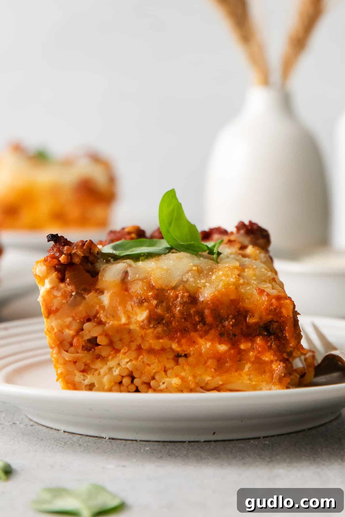 A perfectly portioned slice of golden-brown Million Dollar Spaghetti, showcasing its cheesy layers and hearty meat sauce on a white plate, ready to be enjoyed.