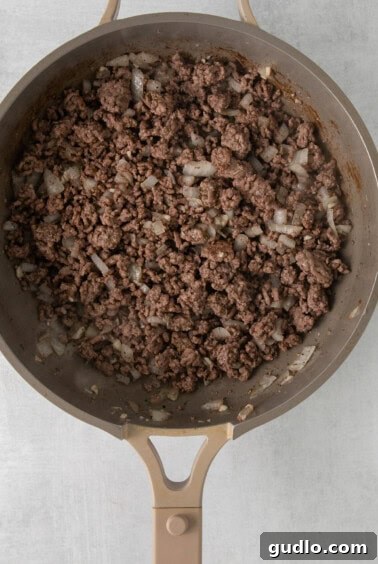 A frying pan filled with seasoned ground beef, sautéed onions, and garlic, ready for marinara.