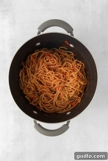 Cooked spaghetti noodles tossed with marinara sauce in a large pot.