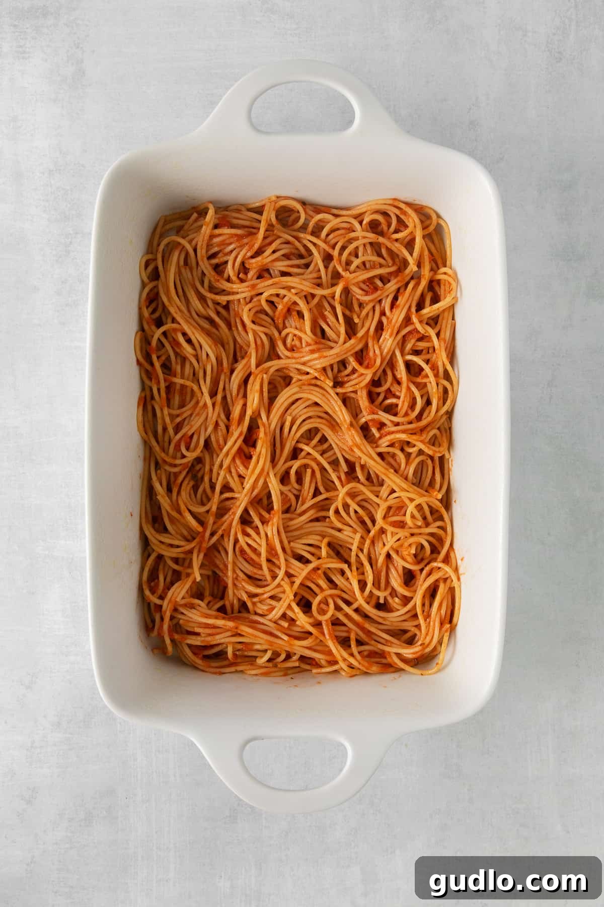 A large baking dish filled with pre-baked Million Dollar Spaghetti, showing the bottom layer of sauced spaghetti and the initial meat sauce layer, before the final cheese topping.