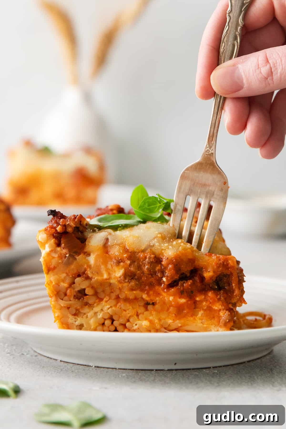 A fork piercing into a hearty slice of Million Dollar Spaghetti, revealing the rich layers of pasta, meat sauce, and melted cheese, ready for a bite.
