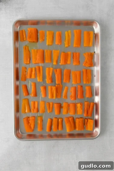 Process of smashing par-boiled carrots on a baking sheet with a glass.