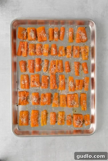Seasoned and parmesan-sprinkled smashed carrots on a baking sheet, ready for the oven.