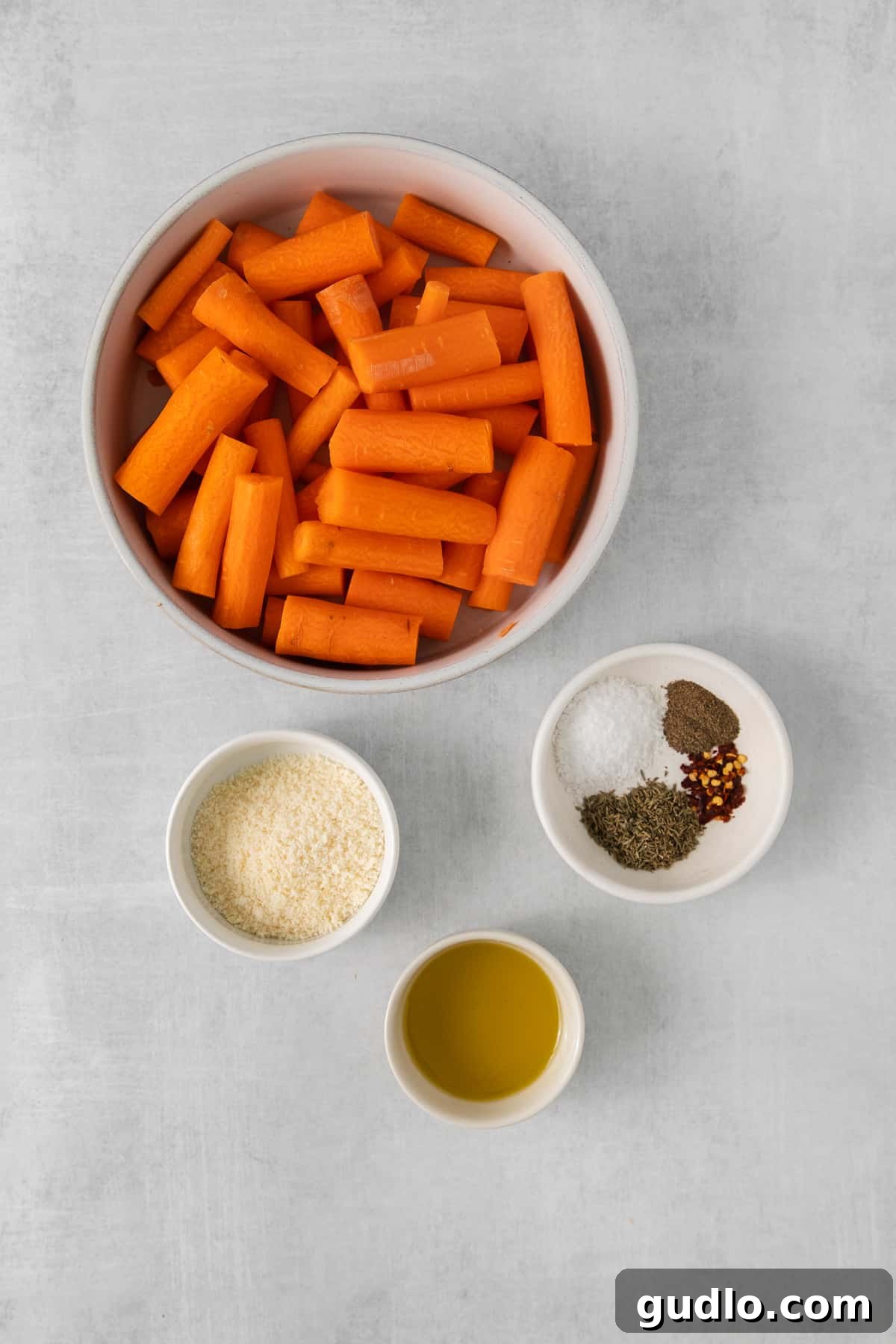 Ingredients for Smashed Carrots and Aioli Bowls of fresh ingredients for Parmesan smashed carrots, including chopped carrots, spices, parmesan cheese, olive oil, and aioli components.