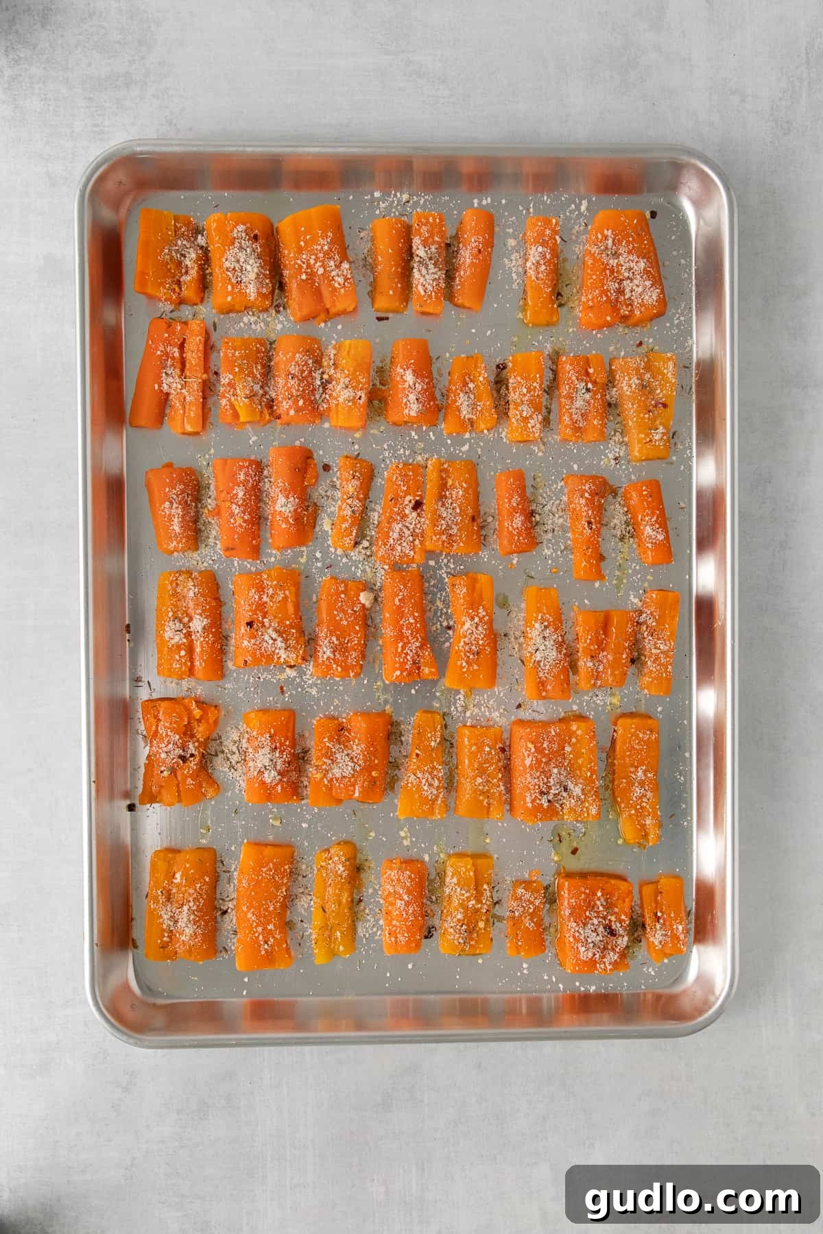 Smashed Carrots on a Baking Sheet Parmesan smashed carrots spread out evenly on a parchment-lined baking sheet, ready for the oven.