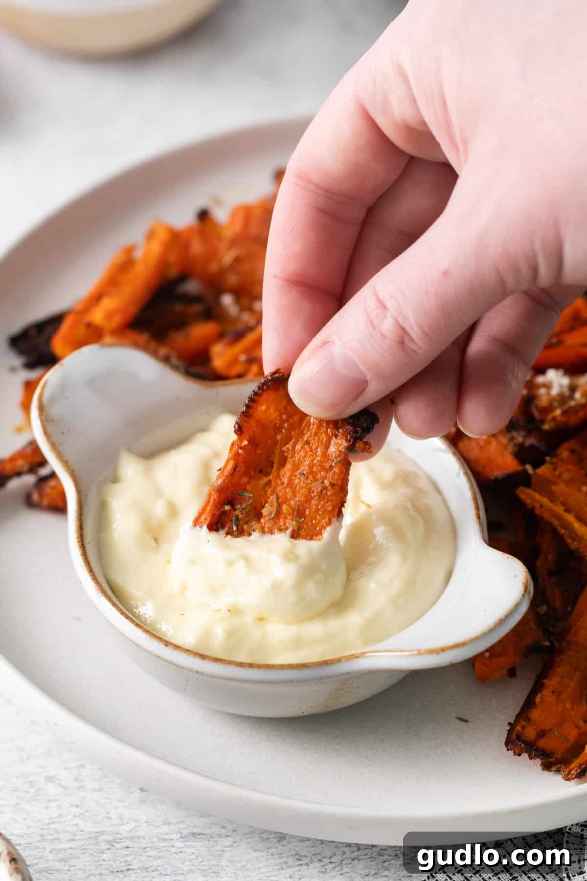 Dipping Smashed Carrots in Aioli A hand gently dipping a crispy Parmesan smashed carrot into a small bowl of creamy aioli.