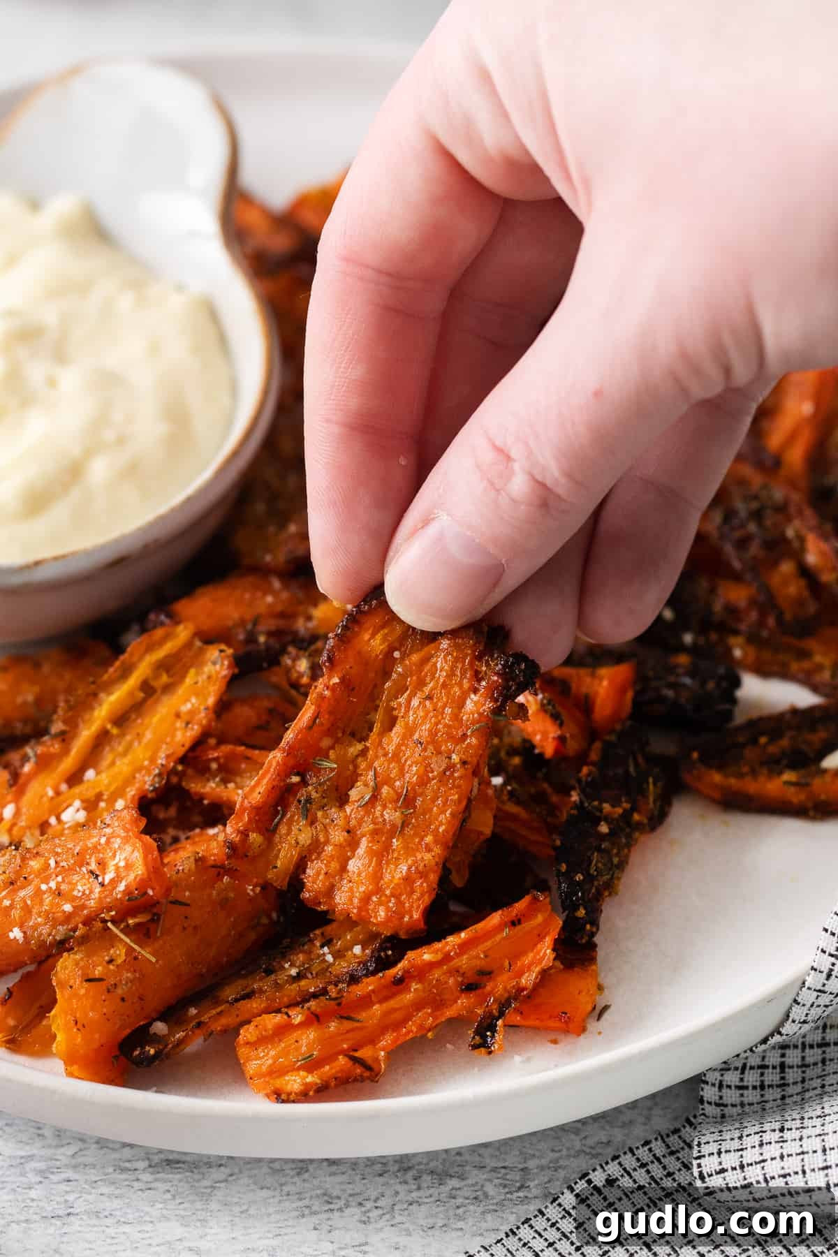 Hand Holding a Smashed Carrot A hand holding a single perfectly baked Parmesan smashed carrot, showing its crispy texture.
