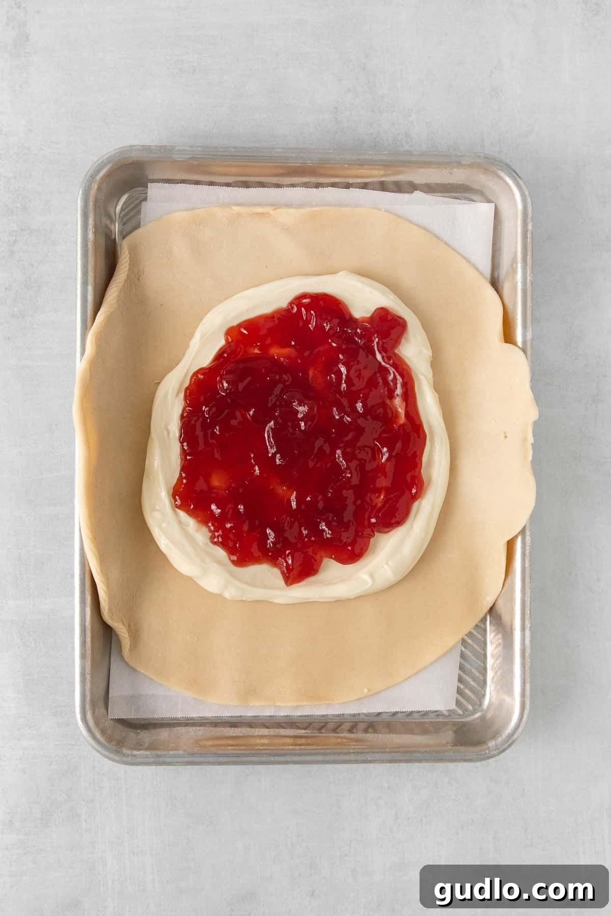 The foundational layers of a strawberry cream cheese tart, featuring a golden pie crust generously spread with a creamy white filling, topped with a glistening layer of vibrant red strawberry jam.