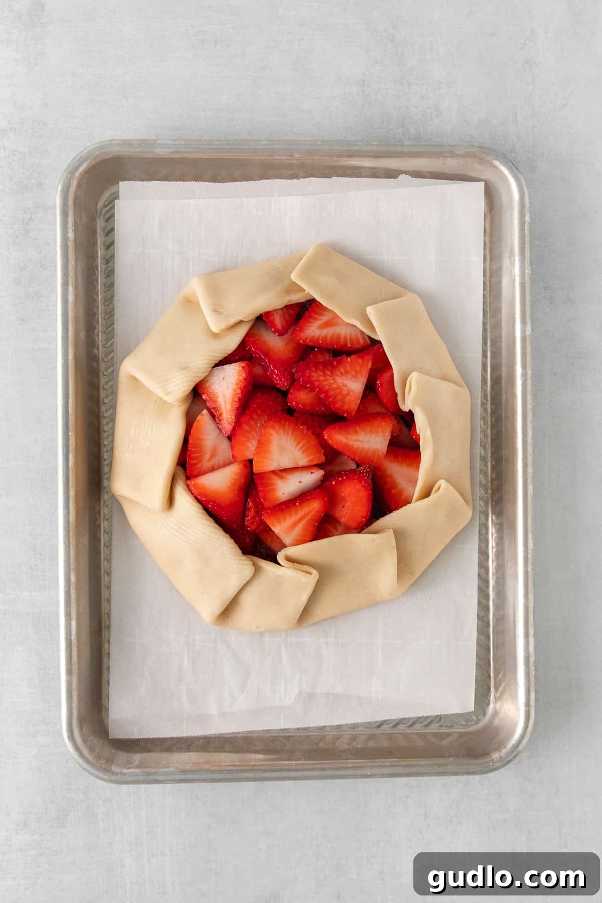 A glorious unbaked strawberry cream cheese tart, showcasing its artfully folded crust and vibrant strawberry topping, resting on a parchment-lined baking sheet, ready for the oven.