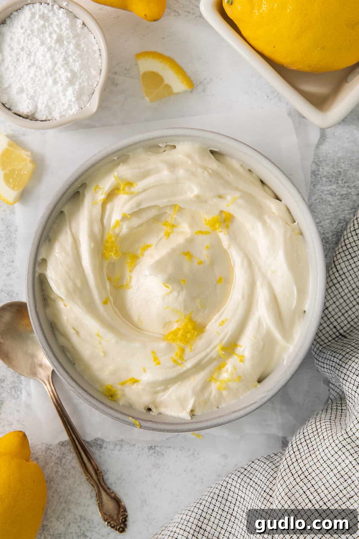 Bright Lemon Cream Cheese Frosting: The Perfect Summertime Topping Lush lemon cream cheese frosting swirled in a pristine white bowl, garnished with delicate lemon zest, ready to be spread.