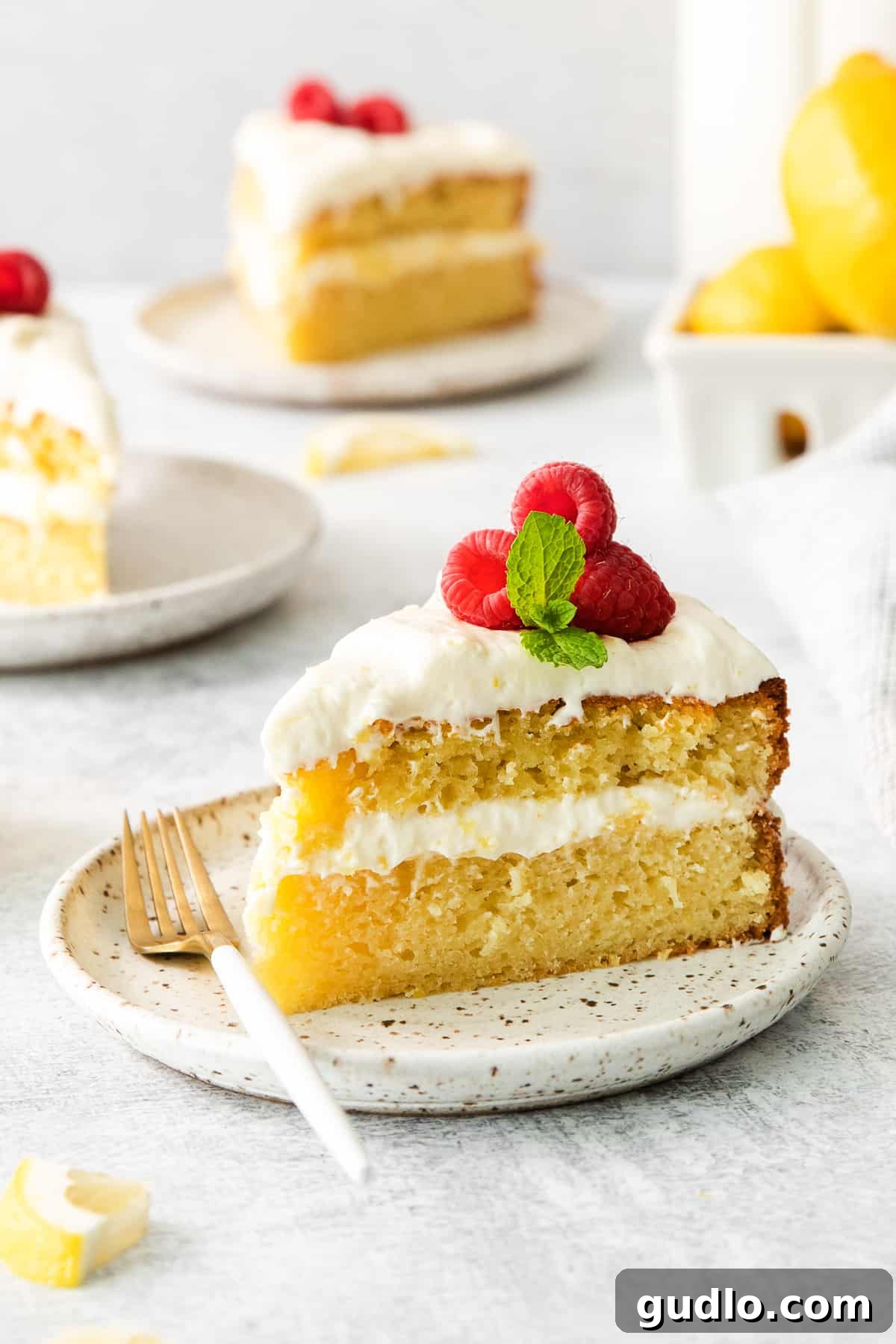 Lemon Cake with Cream Cheese Frosting A perfectly sliced piece of lemon cake, generously frosted with lemon cream cheese frosting, resting elegantly on a white plate.