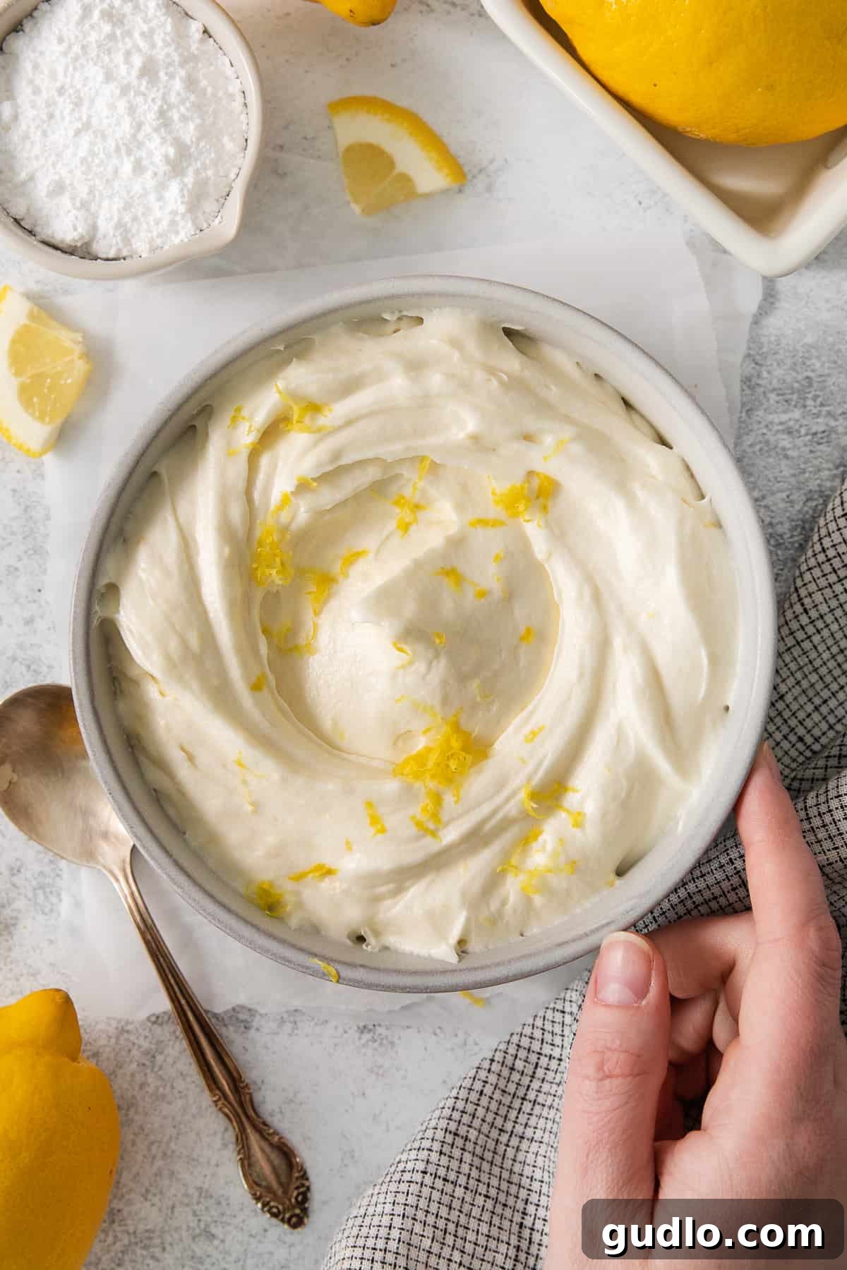Zesty Lemon Cream Cheese Frosting A rustic bowl filled with fluffy lemon cream cheese frosting, beautifully topped with fresh lemon zest, against a warm background.