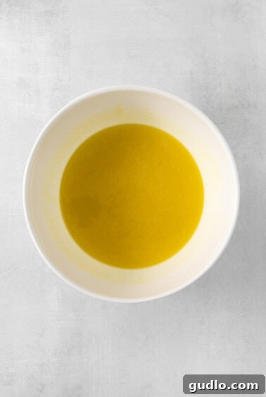 Luminous Lemon Olive Oil Cake 11 Olive oil and granulated sugar being mixed in a white bowl with an electric mixer, demonstrating the start of the wet ingredients preparation.