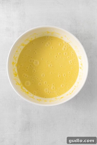 Luminous Lemon Olive Oil Cake 12 A bowl of wet cake ingredients including lemon juice and zest, vanilla, and milk, creating a vibrant yellow liquid mixture.