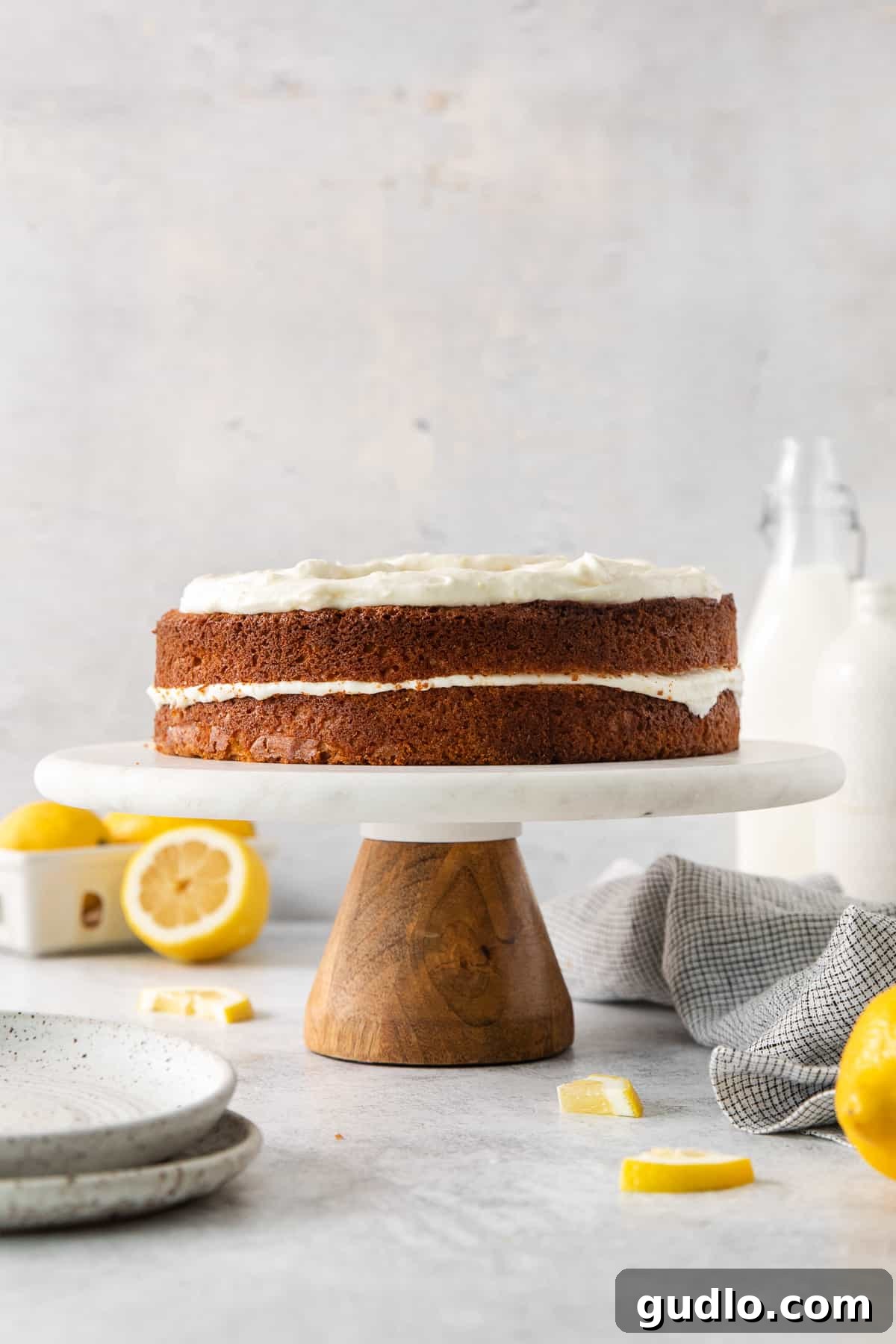 Luminous Lemon Olive Oil Cake 7 A magnificent two-layer lemon olive oil cake, beautifully frosted with lemon cream cheese, standing proudly on a white cake stand, garnished with fresh lemon zest.