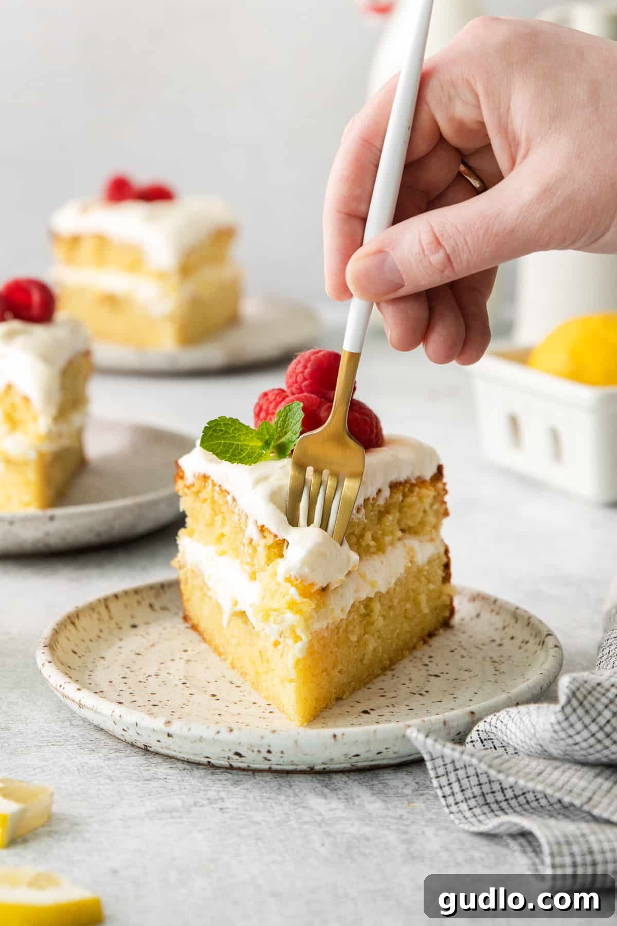Luminous Lemon Olive Oil Cake 9 A tantalizing whole lemon olive oil cake on a white plate, beautifully decorated with lemon cream cheese frosting and fresh lemon zest, ready to be sliced and served.