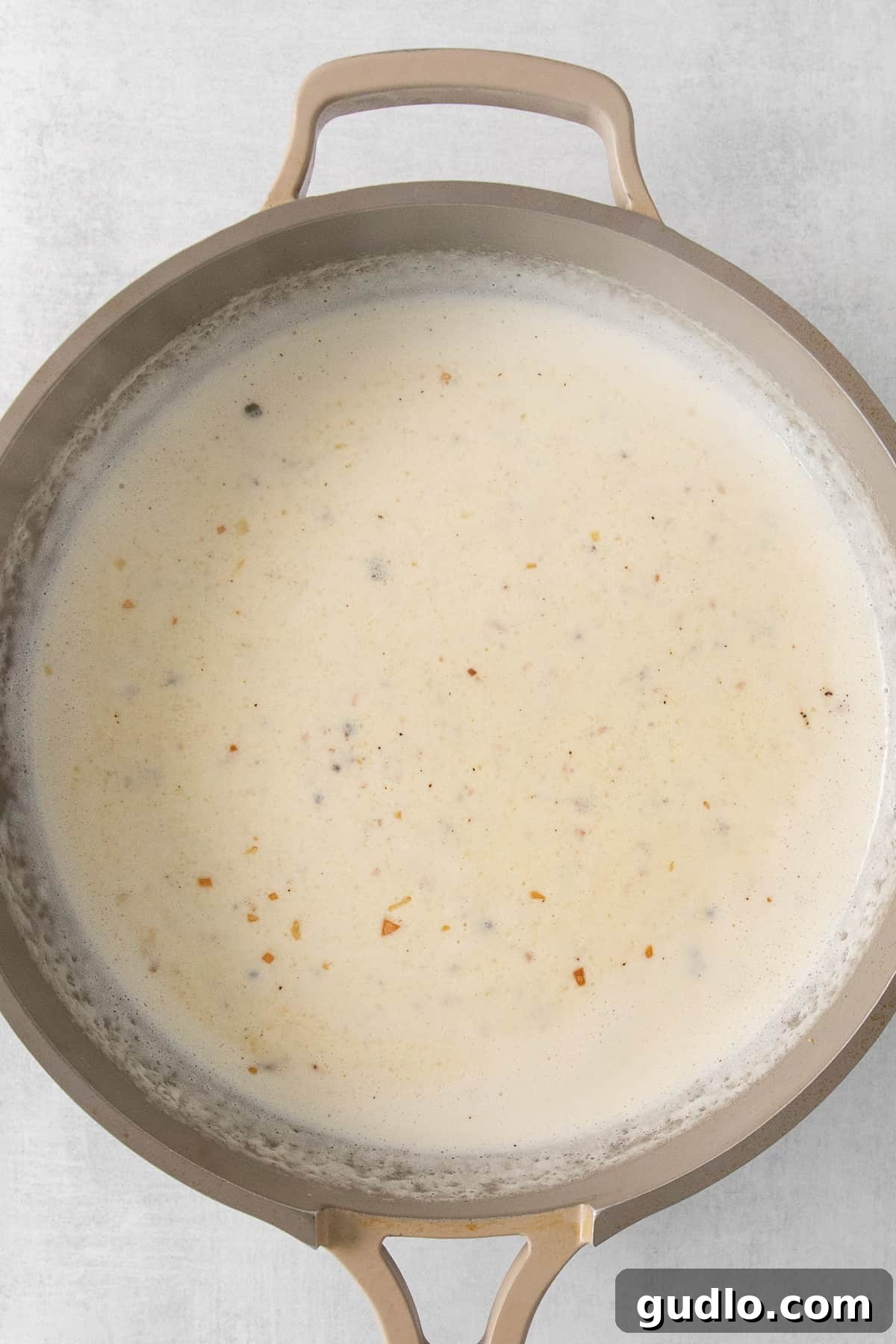 Alfredo Sauce Achieving Perfect Consistency Creamy Alfredo sauce simmering gently in a pan.