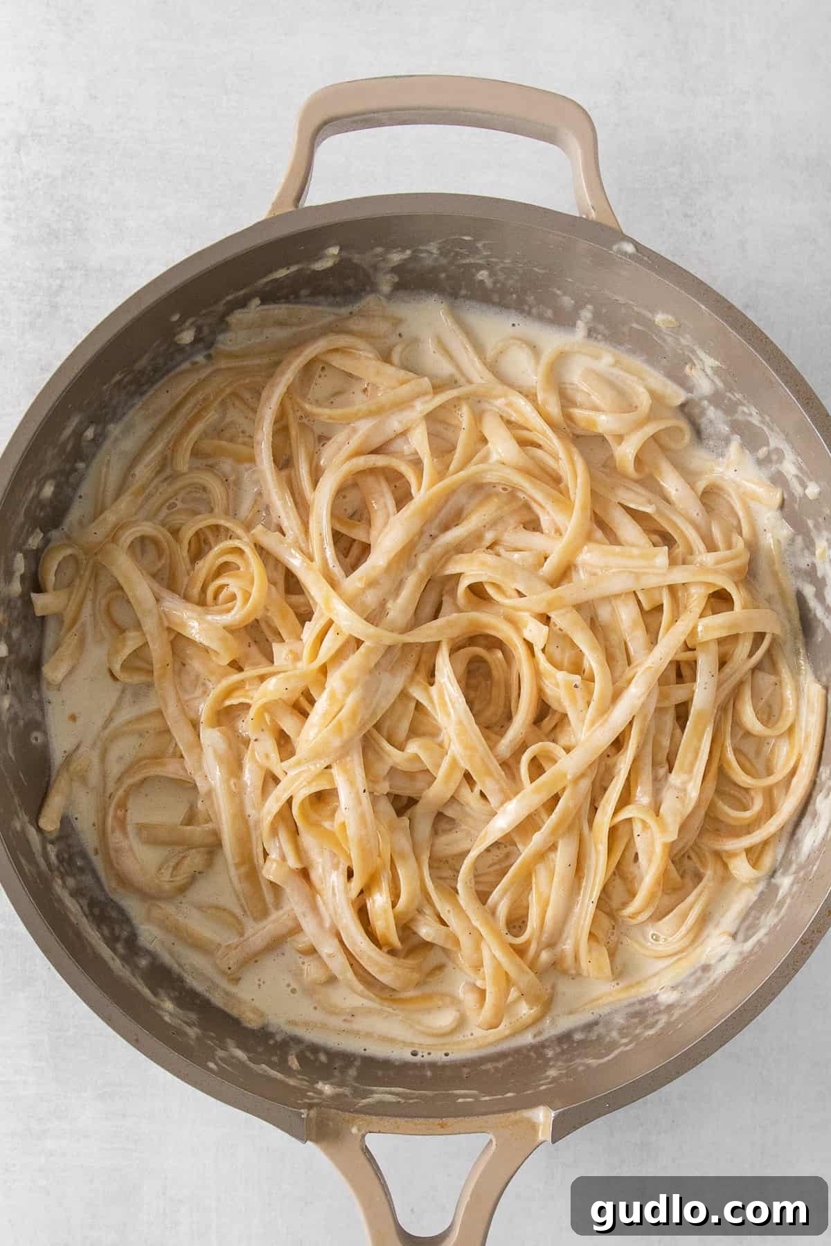 Pasta Gently Tossed in Alfredo Sauce Perfectly cooked pasta tossed in homemade Alfredo sauce in a large pan.