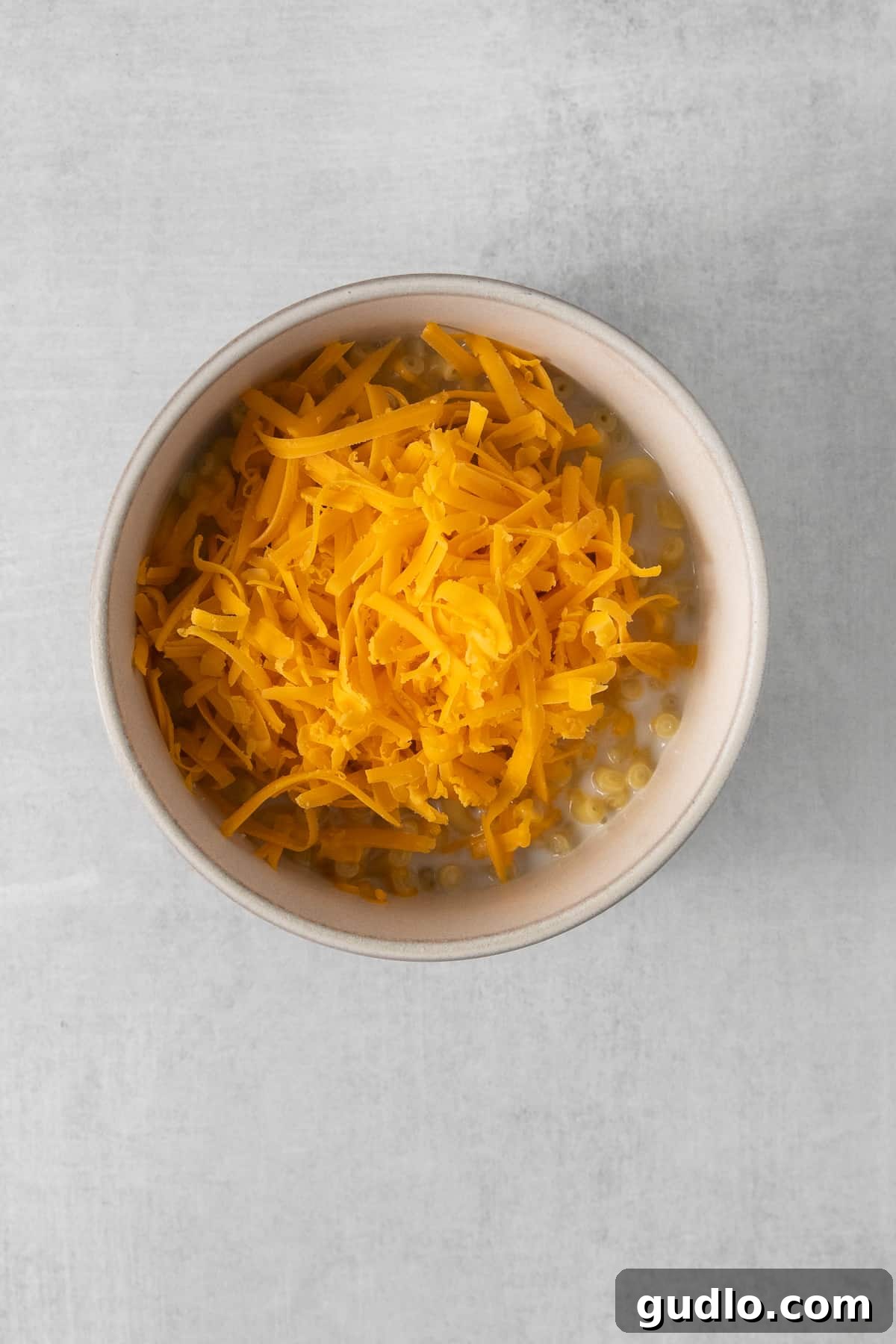 Adding Cheese to Microwave Mac and Cheese Macaroni noodles topped with freshly shredded cheese, pre-melt.