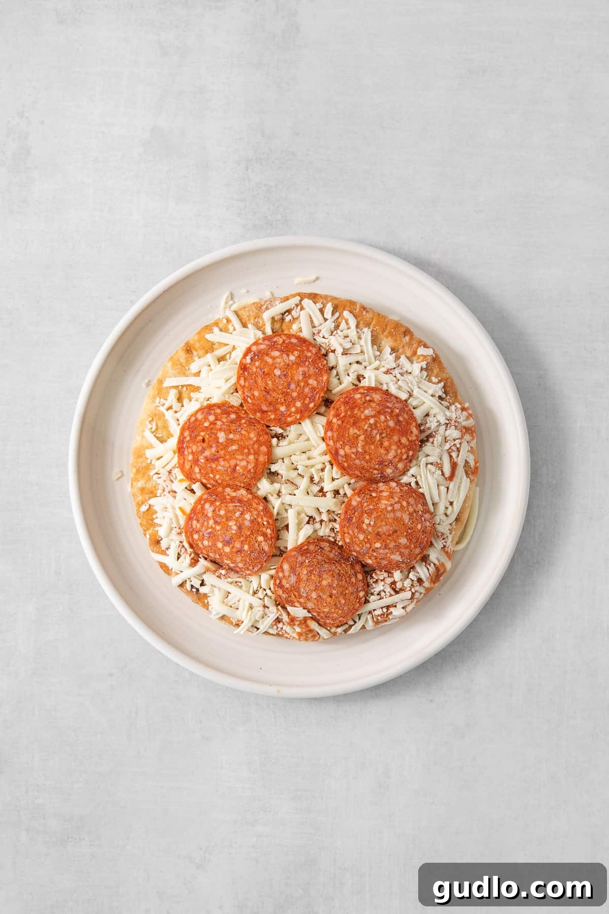 Frozen Pizza Prepped for Air Frying An uncooked frozen pizza ready for the air fryer on a white plate.