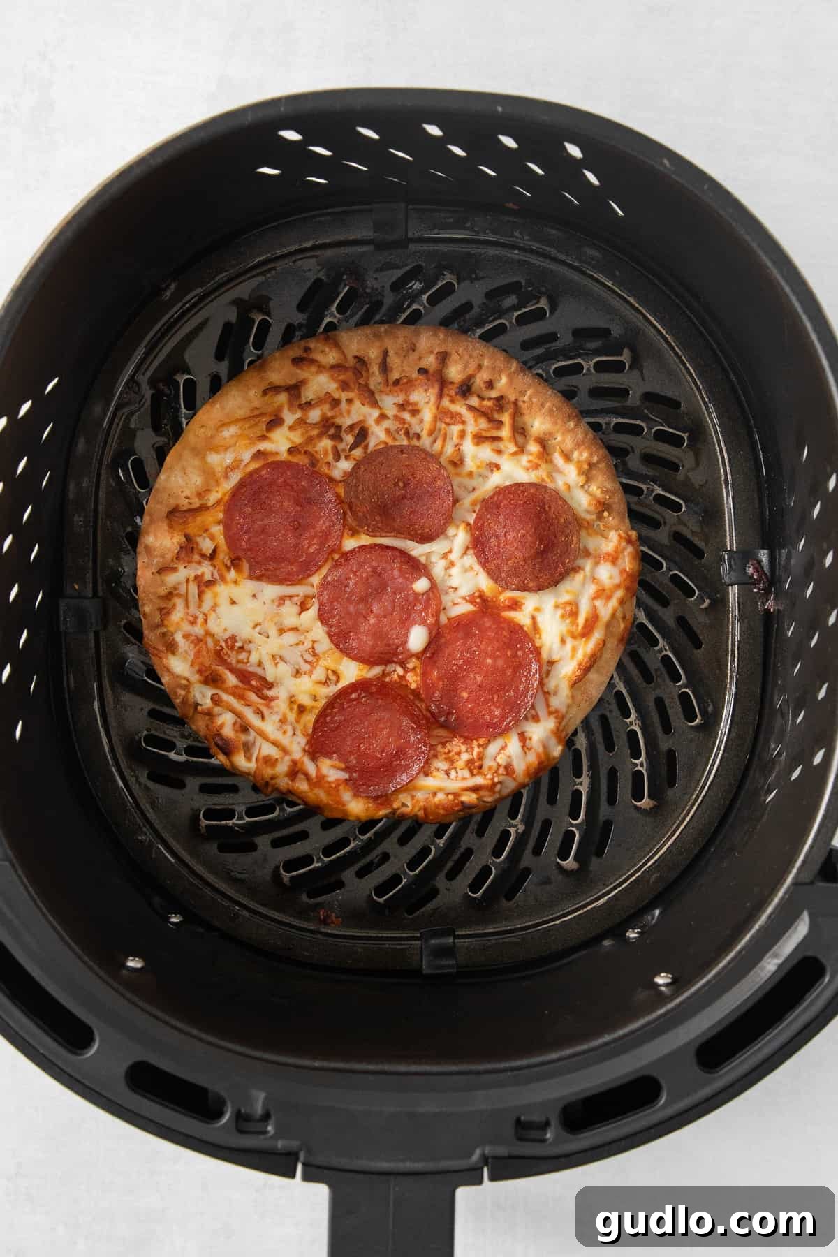 Air Fryer in Action: Pizza Cooking to Perfection A mini frozen pizza perfectly cooking inside an air fryer basket.