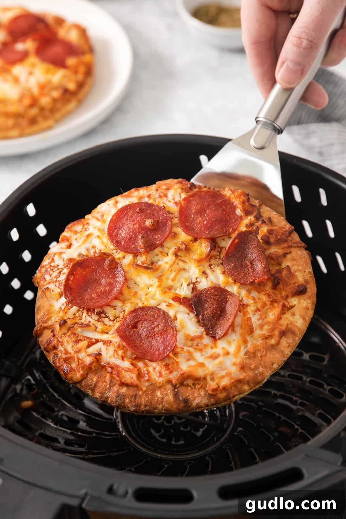 Serving Air Fryer Pizza: Hot and Ready A golden-brown air-fried pizza being lifted from the air fryer basket with a spatula.