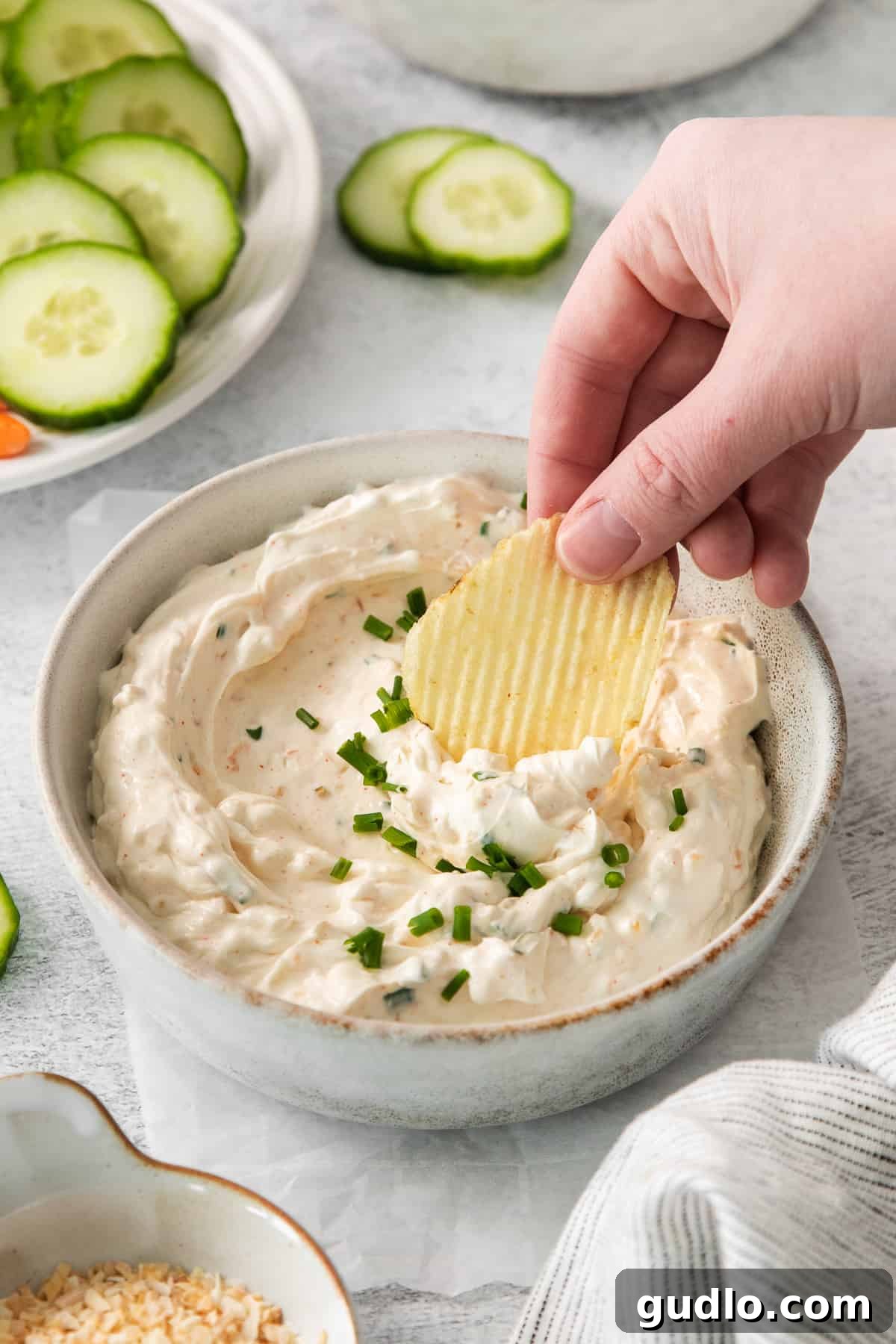 Creamy Homemade Chip Dip A crispy potato chip being perfectly dipped into a bowl of creamy, homemade chip dip, highlighting its enticing texture.