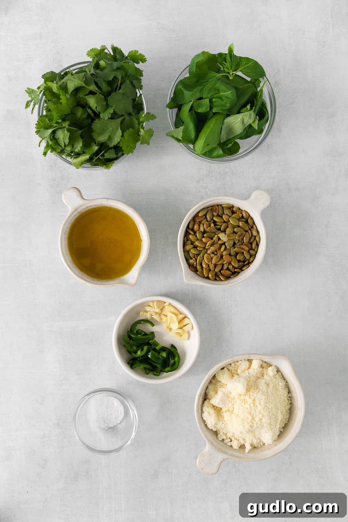 Individual bowls holding ingredients for cilantro pesto: fresh cilantro, basil, pepitas, cotija cheese, garlic, and jalapeño.