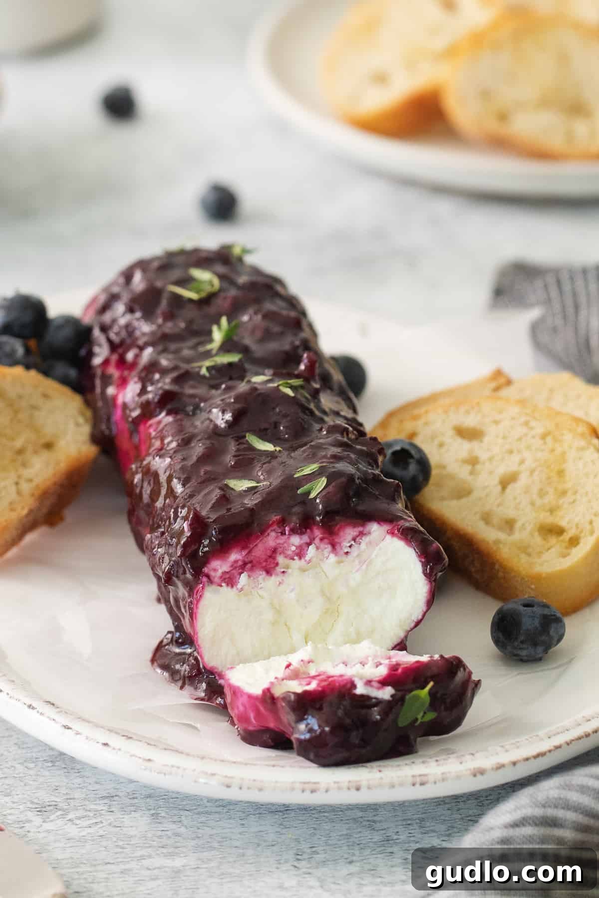 A beautifully presented blueberry goat cheese log on a rustic wooden plate, surrounded by crispy crostini, ready to be served as an elegant appetizer.