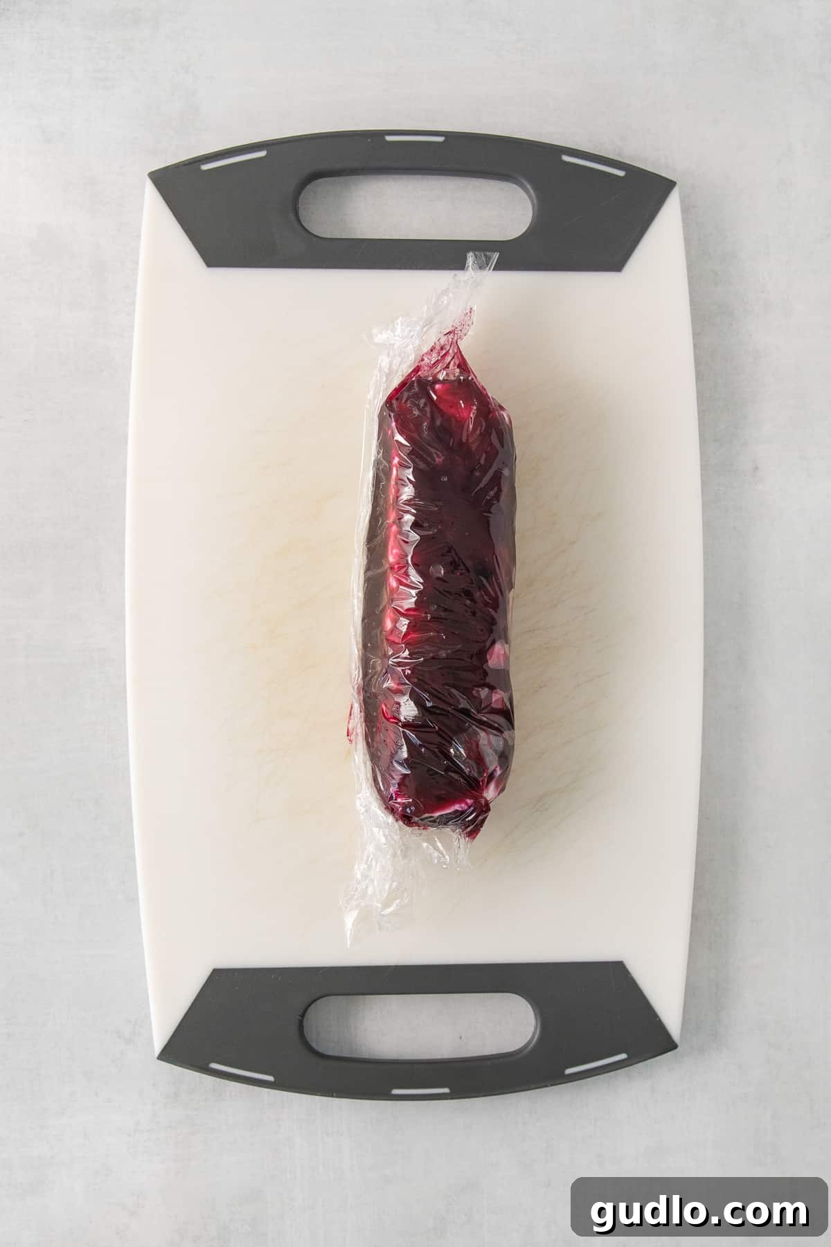 A goat cheese log being carefully rolled and enveloped in the thick blueberry compote using plastic wrap, showing the assembly process for this elegant appetizer.