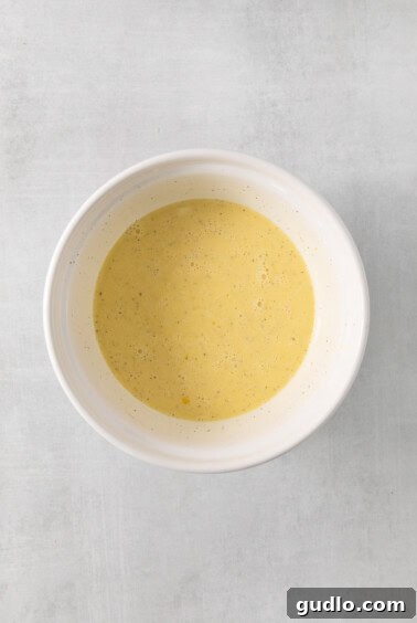 A bowl containing whisked eggs, milk, and cream, ready to form the quiche custard.
