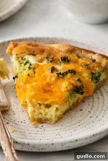 A slice of quiche on a plate, with a fork, ready for tasting.