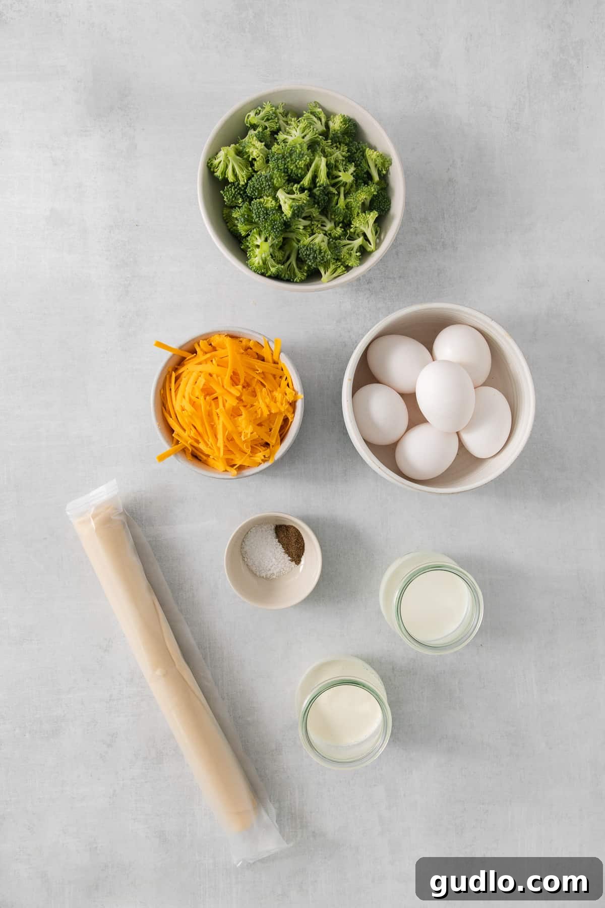 Fresh ingredients laid out on a table, including broccoli florets, shredded cheese, and a pie crust.