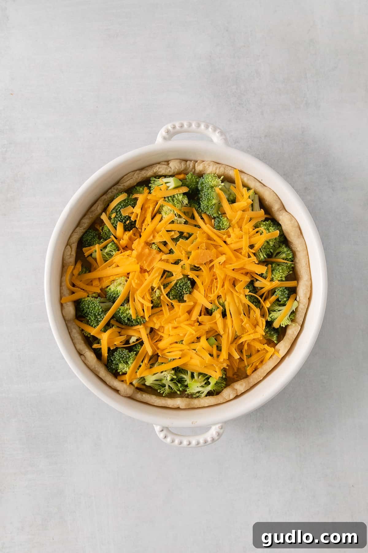 A bowl filled with vibrant broccoli florets and shredded cheddar cheese, ready for quiche assembly.