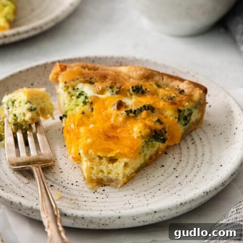 A beautifully presented slice of broccoli cheddar quiche on a plate, with a fork.