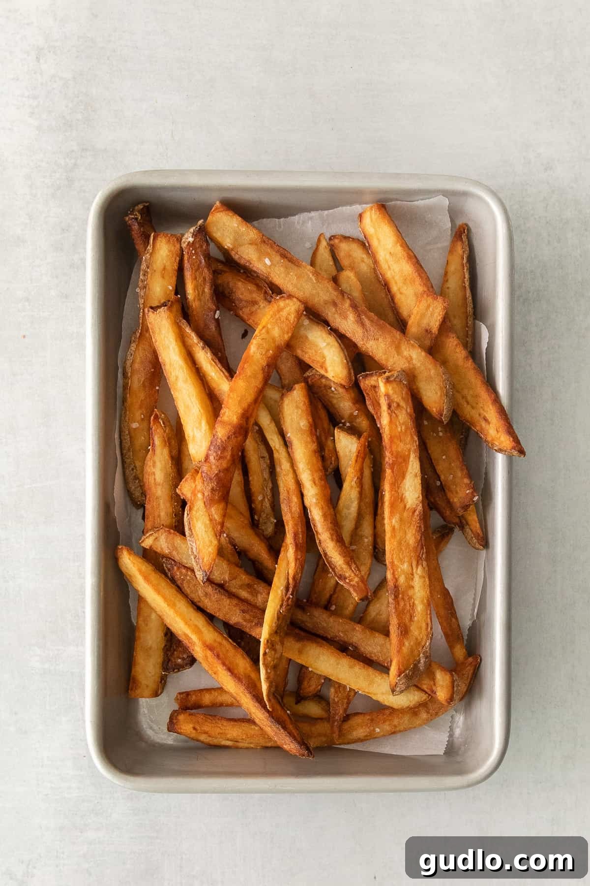 A baking tray laden with golden-brown, crispy French fries, perfectly seasoned and ready for gravy and cheese curds.