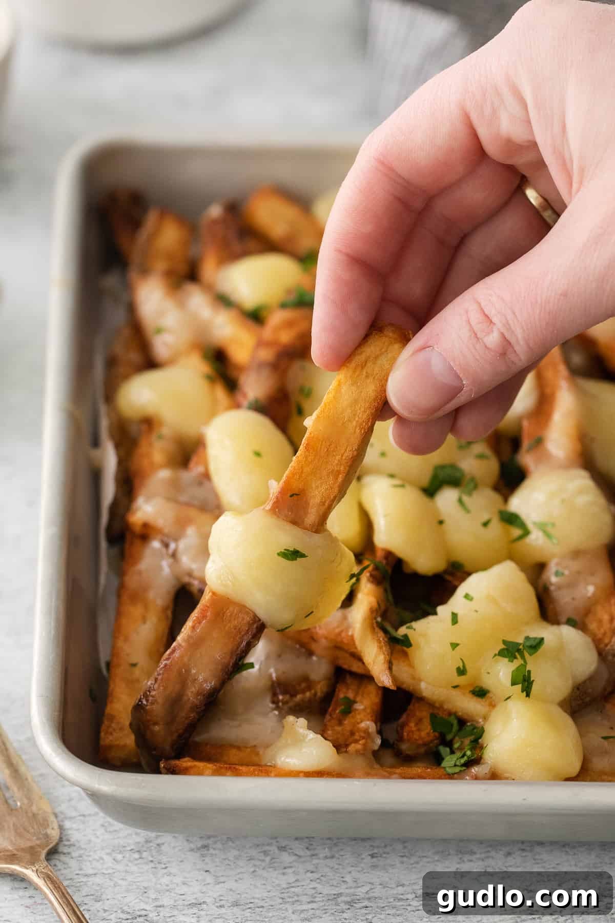 A person dipping a piece of bread into a casserole dish filled with poutine, showing the inviting texture of the gravy and cheese.