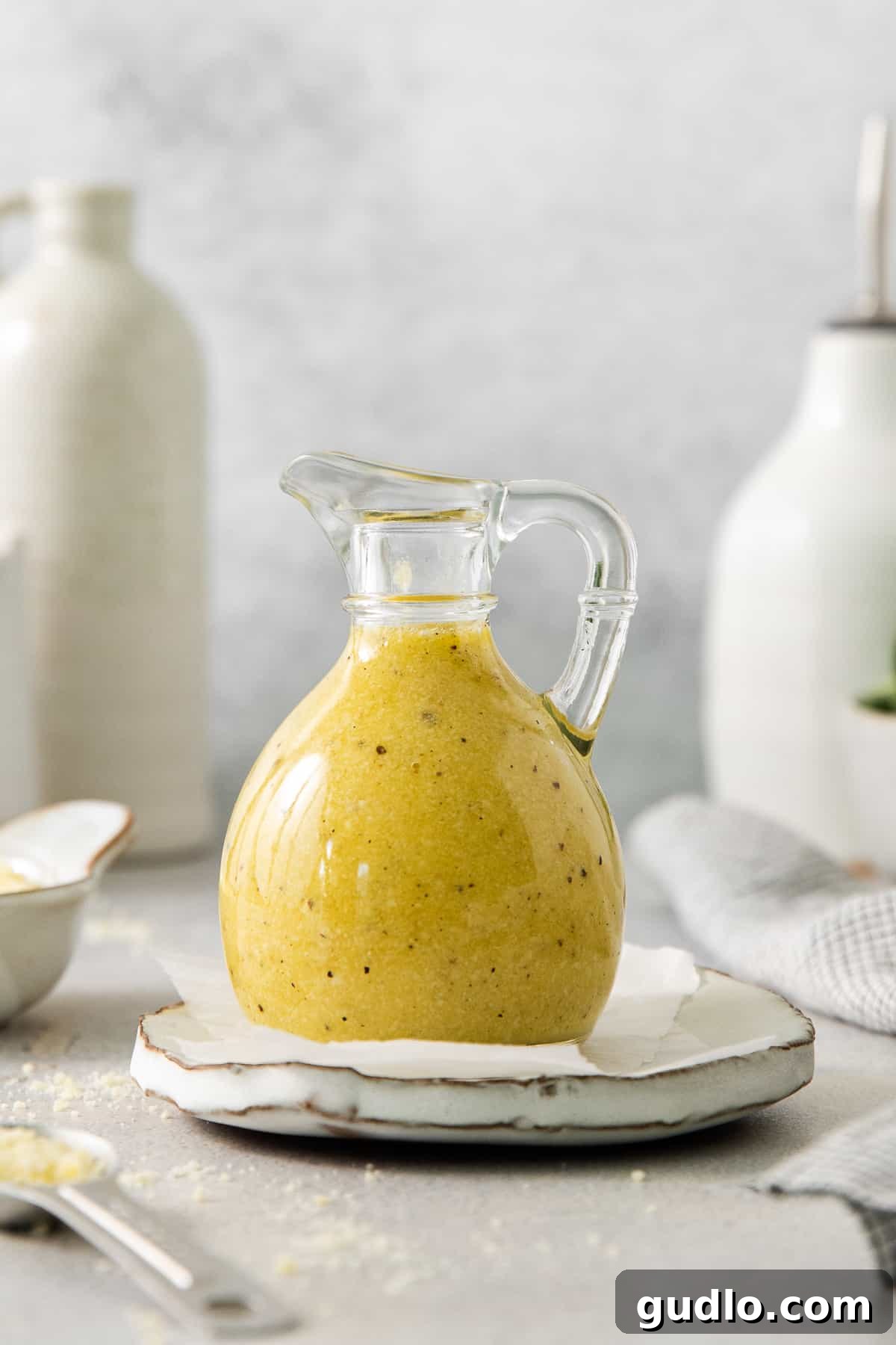 A glass jug of homemade Parmesan cheese dressing, ready to be served, sitting elegantly on a plate.