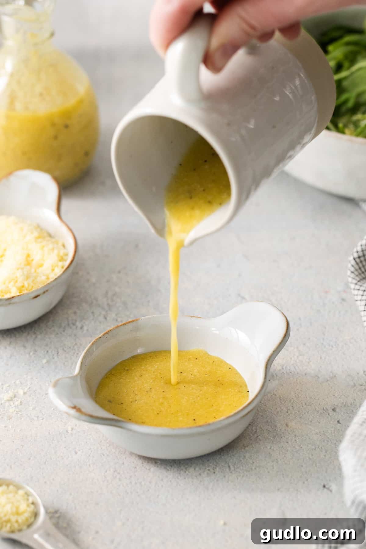 A person expertly pouring the freshly made Parmesan cheese dressing into a serving bowl, ready for drizzling.