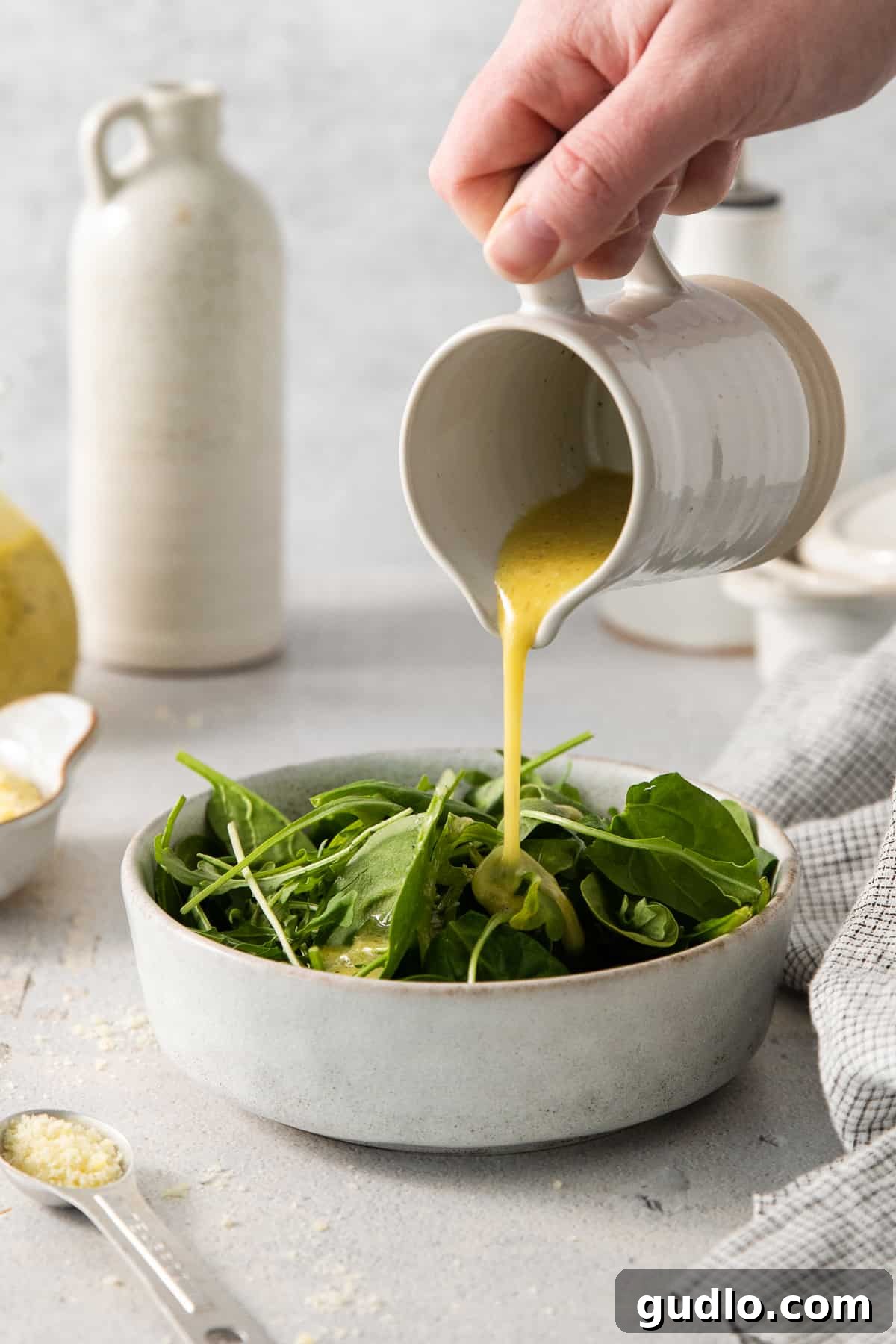 A close-up shot of a person gracefully pouring the creamy Parmesan cheese dressing over a fresh bowl of vibrant green salad.