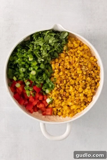 Ultimate Cream Cheese Corn Dip 12 A white bowl filled with corn and vegetables being mixed.