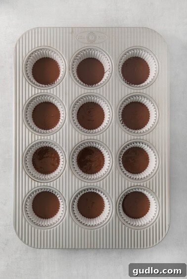 A muffin tin filled with the initial layer of chocolate, forming the base of the homemade Almond Joy candies.