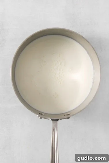 A saucepan filled with milk on a pristine white background, gently heating.