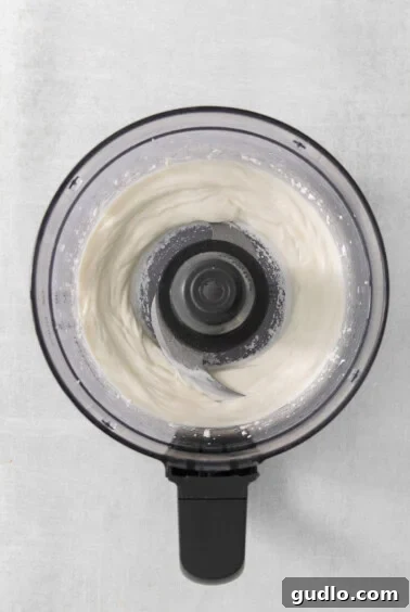 A close-up view of a food processor actively blending curds into a smooth, whipped consistency.