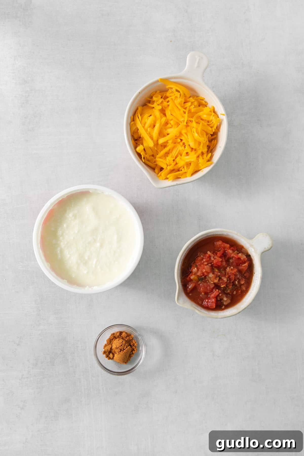 Creamy Protein Cottage Queso 3 Three small bowls, artfully arranged, containing vibrant ingredients for the queso: golden shredded cheese, fresh and colorful pico de gallo, and creamy cottage cheese.