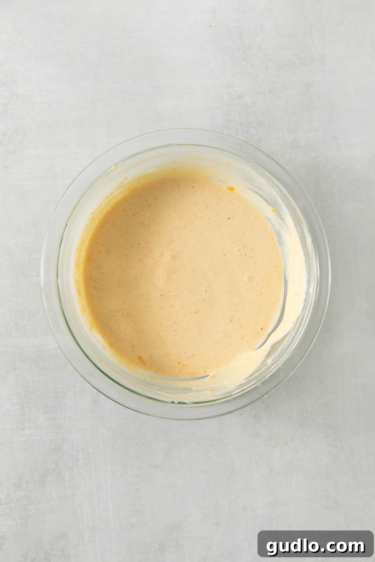 Creamy Protein Cottage Queso 5 A close-up view of a ceramic bowl filled with golden, smooth cottage cheese queso, garnished with vibrant green pico de gallo, ready for dipping.