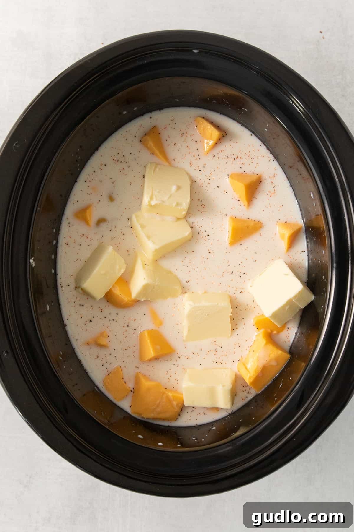 Ultimate Velveeta Crockpot Mac and Cheese 5 a crock pot filled with butter and cubes of cheese.