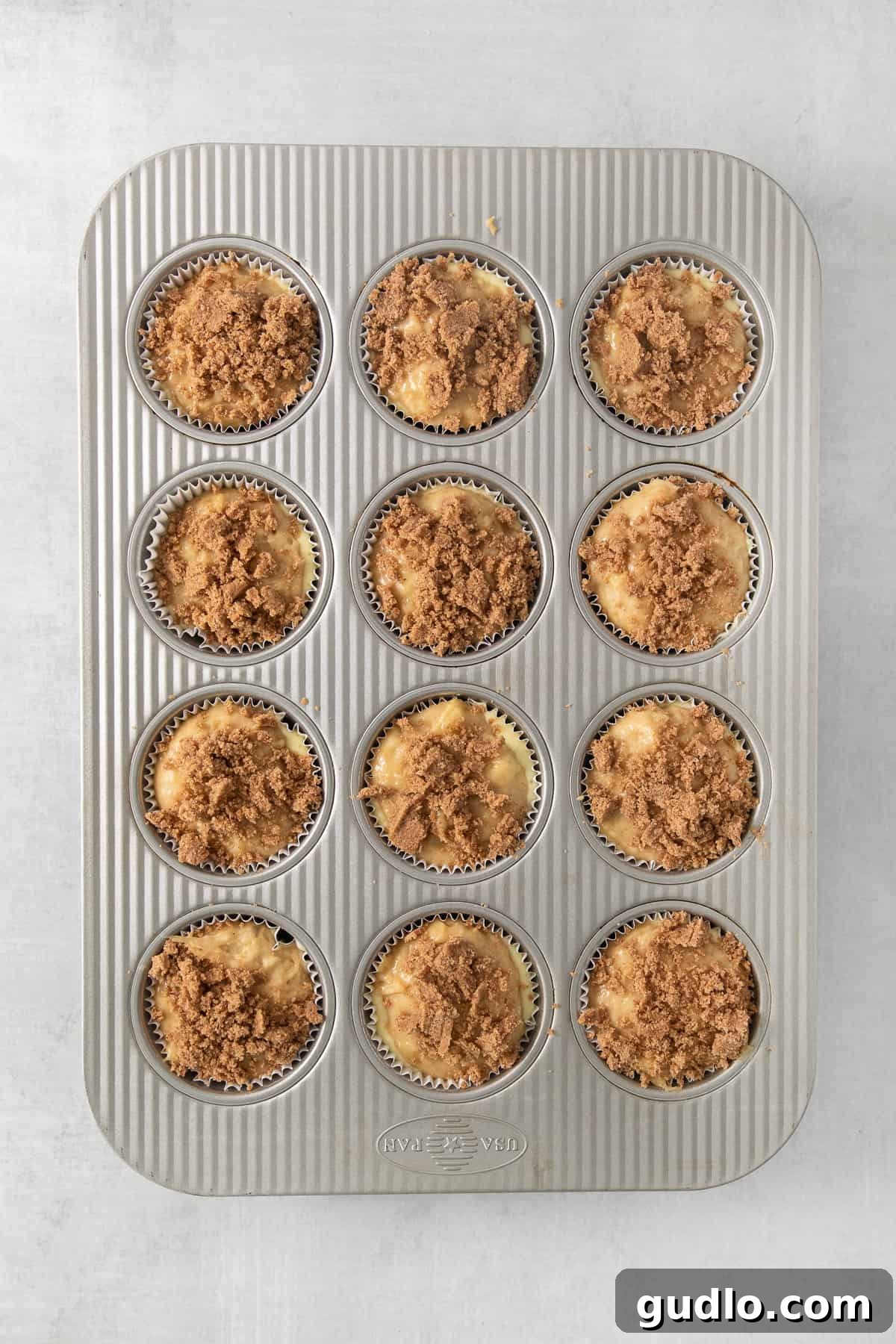 Decadent Cream Cheese Banana Bread Muffins 4 A muffin pan neatly filled with assembled cream cheese banana bread muffins, topped with a generous streusel crumb before baking.
