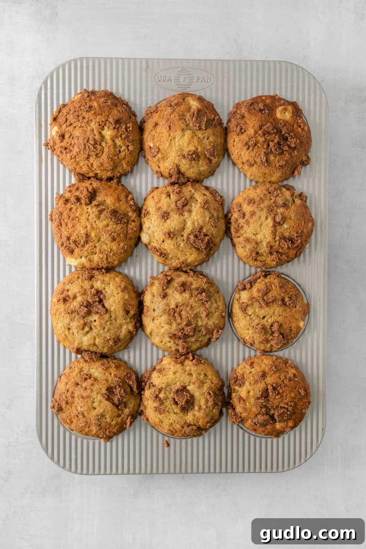 Decadent Cream Cheese Banana Bread Muffins 5 A batch of baked cream cheese banana bread muffins sitting in a metal muffin pan on a grey background, ready to be enjoyed.