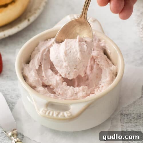 A person expertly scooping luscious strawberry whipped cream cheese into a pristine white bowl, highlighting the creamy texture and vibrant color of the homemade spread.
